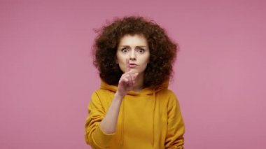 - Sessiz ol! Kapüşonlu kapüşonlu, dudağında parmak olan afro saçlı bir kız sessiz kalmak ve kızgın bir ifadeyle kameraya bakmak istiyor. Pembe arka planda kapalı stüdyo çekimleri