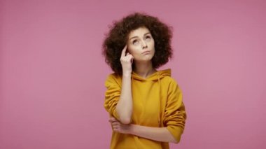 Kapüşonlu akıllı afro saçlı kız parmağını kaldırmayı düşünüyor ve harika bir fikri var. Başparmaklarını kaldırıyor, aniden zekice bir çözüm bulduğuna şaşırıyor. Pembe arka planda kapalı stüdyo çekimleri