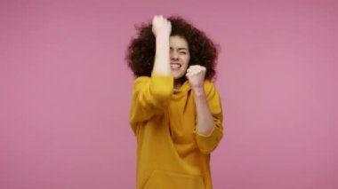 Hevesli, mutlu, afro saçlı, kapüşonlu, neşeli bir kız saçı vardı. Bağırarak, el hareketleriyle yumruk kaldırarak başarıyı, galibiyeti ve gol başarısını kutluyordum. Stüdyo çekimi pembe arkaplanda izole edildi
