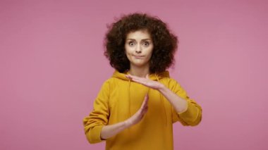 Kapüşonlu, yorgun, afro saçlı, korkmuş bakışları olan, el hareketi yapan, mola isteyen, dinlenmeye ihtiyacı olan bir kız. Pembe arka planda kapalı stüdyo çekimleri