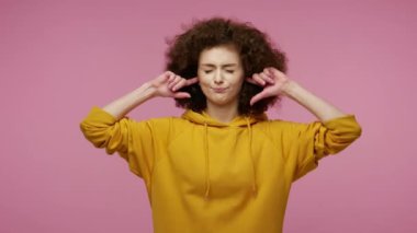 Dinlemek istemiyorum! Kapüşonlu, kulaklarını kapatıp el kol hareketi yapan sinirli, afro saçlı bir kız. Hayır, tavsiyeden kaçınıyor, nahoş sesleri ve yüksek sesleri görmezden geliyor. Stüdyo çekimi pembe arkaplanda izole edildi