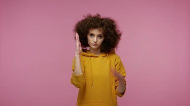 Kapüşonlu şık kız afro saç stili ciddi sakin yüzüyle hafifçe dans ediyor ve dokundurucu hareketler yapıyor, elleri havada, internet mim hareketi yapıyor. Pembe arka planda kapalı stüdyo çekimleri