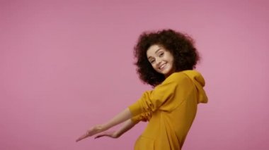 Lütfen, reklama bakın! Kapüşonlu afro saçlı hoş bir kız. Davetiye yapıyor. Promosyon metinleri ve pazarlama için boş yer gösteriyor. Pembe arka planda kapalı stüdyo çekimleri