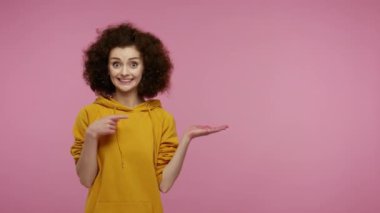 Kapüşonlu afro saçlı hayret verici bir kız avucunun içinde boş bir yeri işaret ediyor, elinde reklam alanının fotokopisini çekiyor, heyecan verici, şaşırmış duygularını ifade ediyor. Pembe arka planda kapalı stüdyo çekimleri