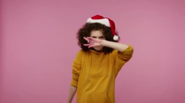 Komik, afro saçlı, Noel Baba şapkalı, dans eden, şarkı söyleyen, gamsız mutlu hisseden enerjik bir şekilde dans eden, Noel partisinde rahatlayan bir kız. Stüdyo çekimi pembe arkaplanda izole edildi