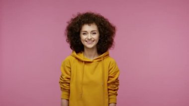 Kapüşonlu afro saçlı aktris kız farklı yüz ifadeleri sergiliyor, gülüyor, şaşırıyor, kırgın görünüyor, aptal surat yapıyor. Pembe arka planda kapalı stüdyo çekimleri