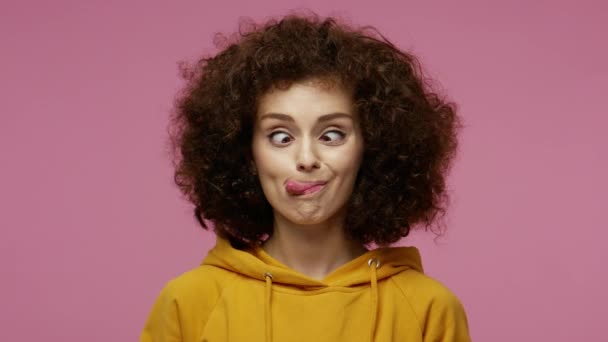 Funny amusing girl afro hairstyle in hoodie looking awkward with crossed eyes and puffed cheeks, fooling around making stupid brainless dumb expression. indoor studio shot isolated on pink background — Stock Footage Funny Amusing Girl Afro Hairstyle Hoodie Looking Awkward Crossed Eyes Royalty Free Stock Footage