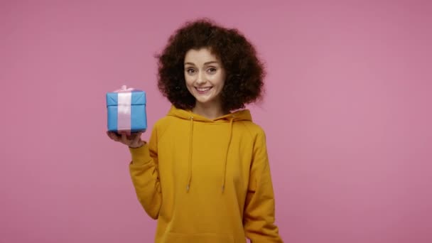 这是给你的礼物迷人的快乐女孩穿着帽衫 指着包装好的礼品盒笑着 庆祝节日 并提供奖金 在粉红背景下隔离的室内拍摄 — 图库视频影像