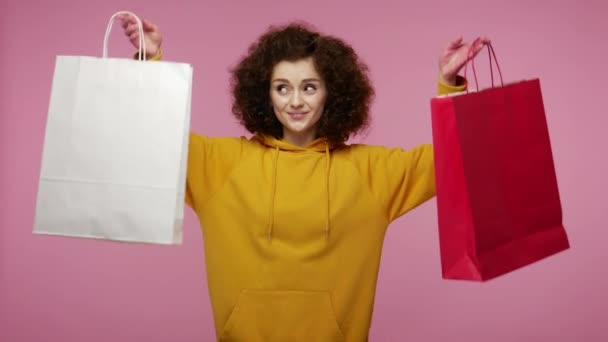 ファッションストアのクライアントの興奮した喜びの感情は 購入に満足して見て 販売を楽しんで 買い物袋を上げるパーカーで笑顔の女の子アフロヘアスタイル ピンクの背景に隔離されたスタジオショット — ストック動画