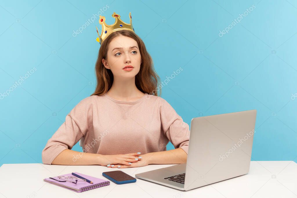 I am big boss. Proud self-confident authoritative businesswoman wearing crown on head, sitting in her office workplace and looking with arrogance. indoor studio shot isolated on blue background