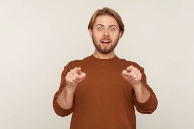 Vay, hey sen! Tişörtlü, eşofman üstü giymiş, kamerayı işaret eden ve şaşırmış bir ifadeyle bir şeye şaşırmış bir adamın portresi. Stüdyoda çekim izole edildi