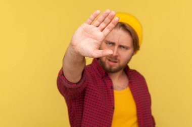 İçki yasağı, inkar konsepti. Şapkalı ve damalı tişörtlü hippi sakallı adam el hareketini durdurdu, uyardı ve reddediyor. Sarı arka planda izole edilmiş kapalı stüdyo çekimi