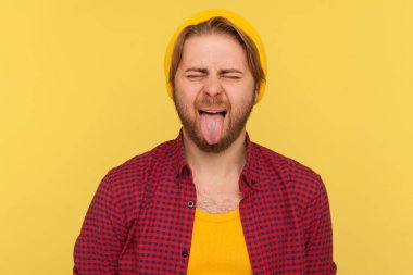 Bereli şapkalı hippi bir adamın portresi. İtaatsiz bir yüz ifadesi takınıyor. Dilini dışarı çıkarıyor. Sarı arka planda izole edilmiş kapalı stüdyo çekimi