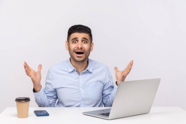 Ofis işyerinde dizüstü bilgisayarı ve kahveyle oturan korkmuş bir adam el kaldırıyor, büyük gözlerle bakıyor korkmuş kızgın ifadeler, stresli bir iş. Stüdyoda çekim izole edildi