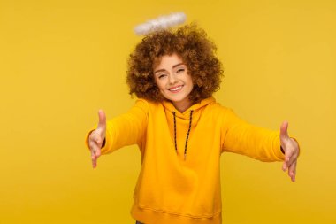 Nazik kalpli, kıvırcık saçlı hippi kadının portresi. Azize nimbusuyla kucaklaşmak için ellerini kaldırıyor. Bedava sarılıyor ve sevgiyle gülümsüyor. Sarı arka planda izole edilmiş kapalı stüdyo çekimi