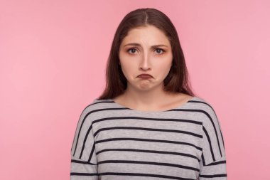 Üzüntü, olumsuz duygular. Çizgili tişörtlü mutsuz genç bir kadının portresi hayal kırıklığına uğramış bir ifadeyle, dargın bir suratla bakıyor. Pembe arka planda kapalı stüdyo çekimleri