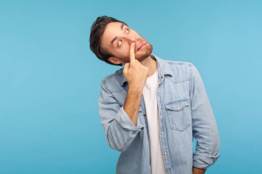Misconduct, bad manners. Portrait of funny crazy man in worker denim shirt picking nose and sticking out tongue with dumb comical expression, fooling around. studio shot isolated on blue background