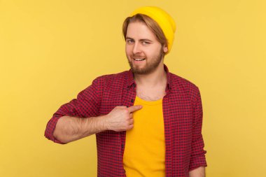 En iyisi benim! Kendine güveni tam, şapkalı ve damalı gömlekli sakallı hippi gururlu kibirli bencil kameraya bakıyor. Stüdyo çekimi sarı arkaplanda izole edildi