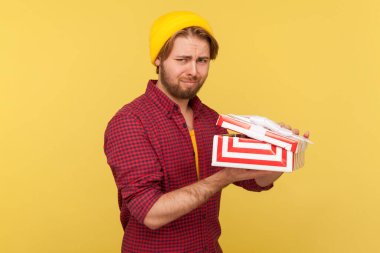 Bereli şapkalı, kareli tişörtlü üzgün adam hediye kutusunu açtı ve kameraya baktı. Hayal kırıklığına uğramış, berbat doğum günü hediyesinden memnun kalmamış. Stüdyo çekimi sarı arkaplanda izole edildi