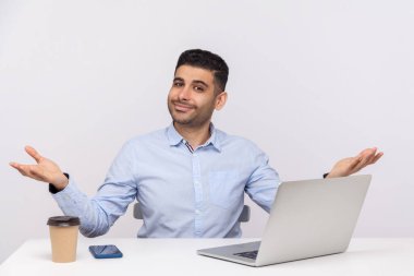 Hoş geldin ve sarıl bana! Dost canlısı, mutlu iş adamı masa başında dizüstü bilgisayarla iş yerinde oturuyor, kucaklaşmak için ellerini sonuna kadar açık tutuyor, müşteriyi selamlıyor. Beyaz arka planda izole edilmiş kapalı stüdyo çekimi