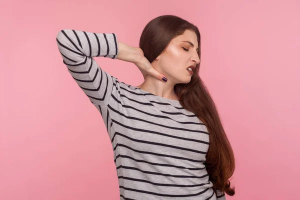 Hurting shoulders, stiff muscles. Portrait of tired sick woman in striped sweatshirt feeling unwell, massaging sore neck, having spinal problems of overwork. studio shot isolated on pink background