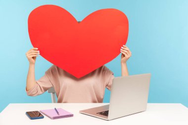 Büyük kırmızı kağıt kalbin arkasına saklanan bir kadın, aşkın sembolü, romantik duygular, dizüstü bilgisayardaki anonim flört servisi, online sohbet ve web sitesi. Mavi arka planda kapalı stüdyo çekimleri