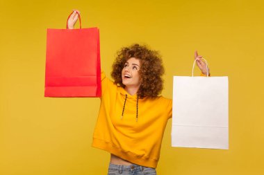 Kapüşonlu mutlu kıvırcık saçlı hippi kız portresi boş alanlı alışveriş torbaları, reklam metinleri için paketlerde kopya alanı. İç mekan stüdyo çekimi, moda mağazası reklamı.
