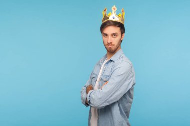 Ben kralım! Altın taç giyen, kibirle bakan, otoritesini ve liderliğini ilan eden, üstün ayrıcalıklı statüsündeki kendinden emin hırslı bir adamın portresi. Stüdyo çekimi mavi arkaplanda izole edildi