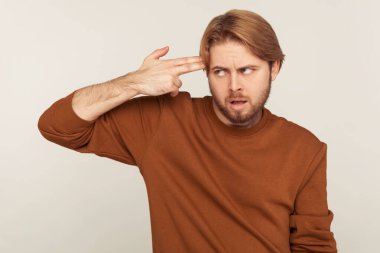 Depresyon, intihar hareketi. Sinirli sakallı bir adamın portresi. Parmak tabancasıyla kafasına doğrultulmuş, kendini tabancayla vuruyor. Gri arka planda kapalı stüdyo çekimi