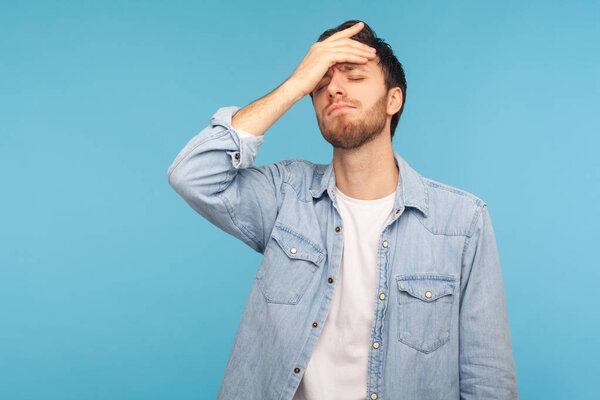 I forgot, my fault. Portrait of upset man in worker denim shirt standing with facepalm gesture, blaming himself, feeling sorrow regret because of bad memory. studio shot isolated on blue background