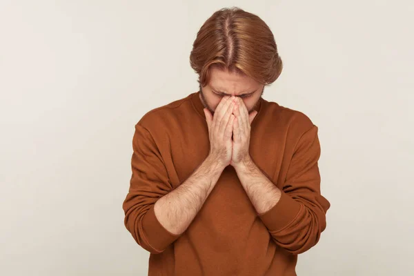 Portrait of upset crying man bowing head wiping tears, hiding face and suffering depression, feeling desperate sorrow, worrying about troubles or bereavement. studio shot isolated on gray background