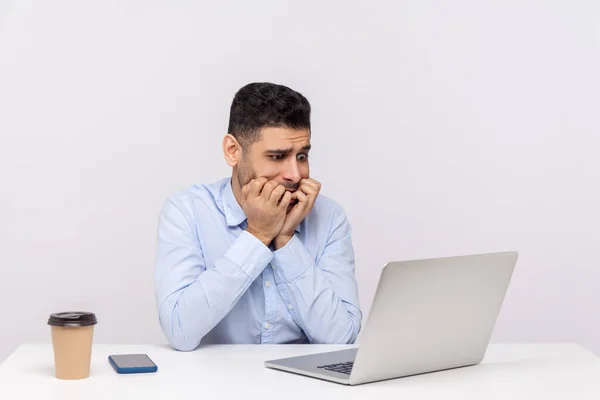 焦虑不安的男性员工坐在办公室的工作场所 焦虑不安地看着笔记本电脑屏幕和咬钉子 慌乱的截止日期 工作上的麻烦 在白色背景下被隔离的工作室拍摄 — 图库照片