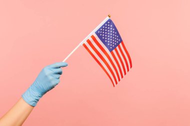 ABD bayrağı taşıyan mavi eldivenli insan elinin profil yan görüntüsü. Amerika Birleşik Devletleri. Ulusal Bağımsızlık Günü - 4 Temmuz. Kapalı, pembe arka planda izole..