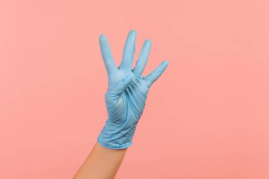 Profil yan görüntüsü. Mavi eldivenli insan eli. Dört numarayı eliyle gösteriyor. İçerde, stüdyoda, pembe arka planda izole edilmiş..