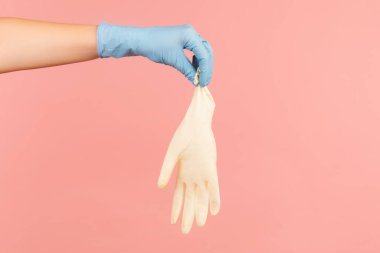 Profil yan görüntüsü, beyaz eldivenli mavi eldivenli insan eli. İçerde, stüdyoda, pembe arka planda izole edilmiş..