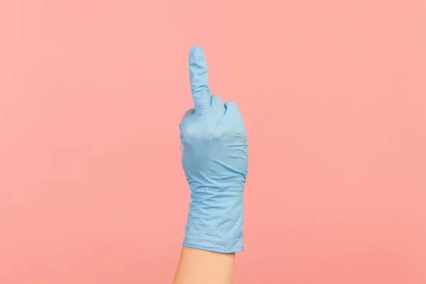 Profile side view closeup of human hand in blue surgical gloves showing middle finger. indoor, studio shot, isolated on pink background.