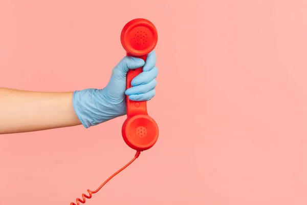 人手侧视特写 手持蓝色手术手套 显示红色电话听筒 演播室拍摄 粉红色背景隔离 — 图库照片