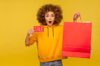 Şok olmuş kıvırcık saçlı kapüşonlu hippi kızın portresi. Elinde alışveriş torbaları ve reklam metni için boş bir alan tutuyor ve satılık yazıları gösteriyor. Moda mağazasının reklamı.