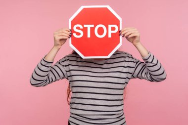 Yasaktır! Çizgili kazak giyen, yüzünü Dur sembolü ile kaplayan, kırmızı trafik işareti taşıyan ve yasak giriş uyarısı yapan isimsiz bir kişinin portresi. Kapalı stüdyo çekimi, pembe arkaplan