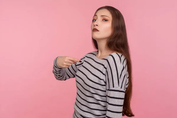 This is me! Portrait of arrogant woman in striped sweatshirt pointing herself and looking selfish egoistic haughty, feeling proud of own achievement. indoor studio shot isolated on pink background