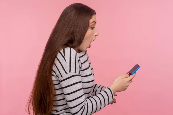 携帯電話で入力し ショッキングなブログを読み ソーシャルネットワークでチャットし モバイルアプリに驚き 不信仰反応の驚きの若い女性のサイドビュー ピンクの背景に隔離された屋内スタジオで — ストック写真