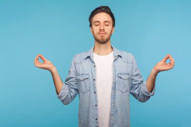 Huzurlu zihin, rahatlama, kot gömlekli sakin adam portresi kapalı gözler ve mudra jesti, meditasyon, konsantre düşünceler. Mavi arka planda kapalı stüdyo çekimleri