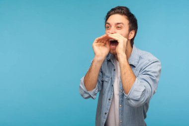 Dikkat, önemli mesaj! İşçi kot gömleği giymiş saldırgan bir adamın portresi megafon şeklinde ellere doğru bağırarak duyuru yapıyor. Mavi arka planda kapalı stüdyo çekimleri