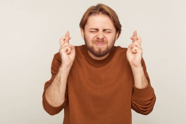 Kader lütfen gel! Tişörtlü sakallı bir adamın portresi şans dilemek için şans diliyor, dua ediyor ve mucize umuyor. Stüdyo çekimi gri arkaplanda izole edildi