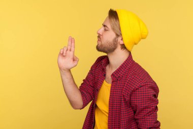 Bereli ve damalı tişörtlü tehlikeli holigan hippi adam parmak tabancasını doğrultuyor, dumandan dumana üflüyor, silah hareketiyle öldürmekle tehdit ediyor. Stüdyo çekimi sarı arkaplanda izole edildi