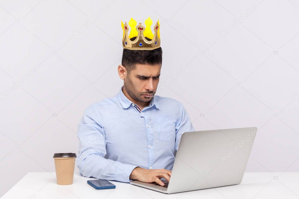 I'm boss! Ambitious arrogant top manager, office employee with crown on head working on laptop and frowning bossy, feeling proud of his position at work. studio shot isolated on white background