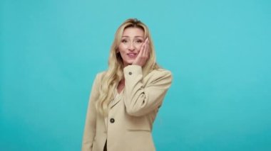 İş ceketli aşırı heyecanlı sarışın kadın yüksek sesle gülüyor, kaygısız pozitif bayan eğleniyor, iyi ruh hali içinde. Mavi arka planda kapalı stüdyo çekimi