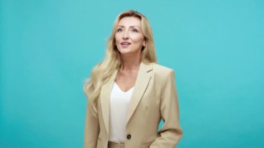 İş elbisesi giymiş orta yaşlı sarışın bir kadından ilham aldım. Geleceği planlayıp, hayal ediyorum. Memnun ve motive olmuş. Mavi arka planda kapalı stüdyo çekimi