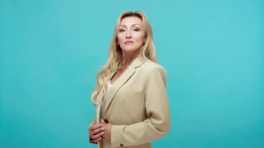 Kendine güveni tam, iş stili ceketli, kendini beğenmiş, gösteriş meraklısı yetişkin bir kadın, lider. Mavi arka planda kapalı stüdyo çekimi