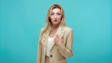 Kim? Ben mi? Hayal kırıklığına uğramış, sarı saçlı, takım elbiseli bir kadın kendine inanamıyor ve zaferini hayretle soruyor. Mavi arka planda kapalı stüdyo çekimi